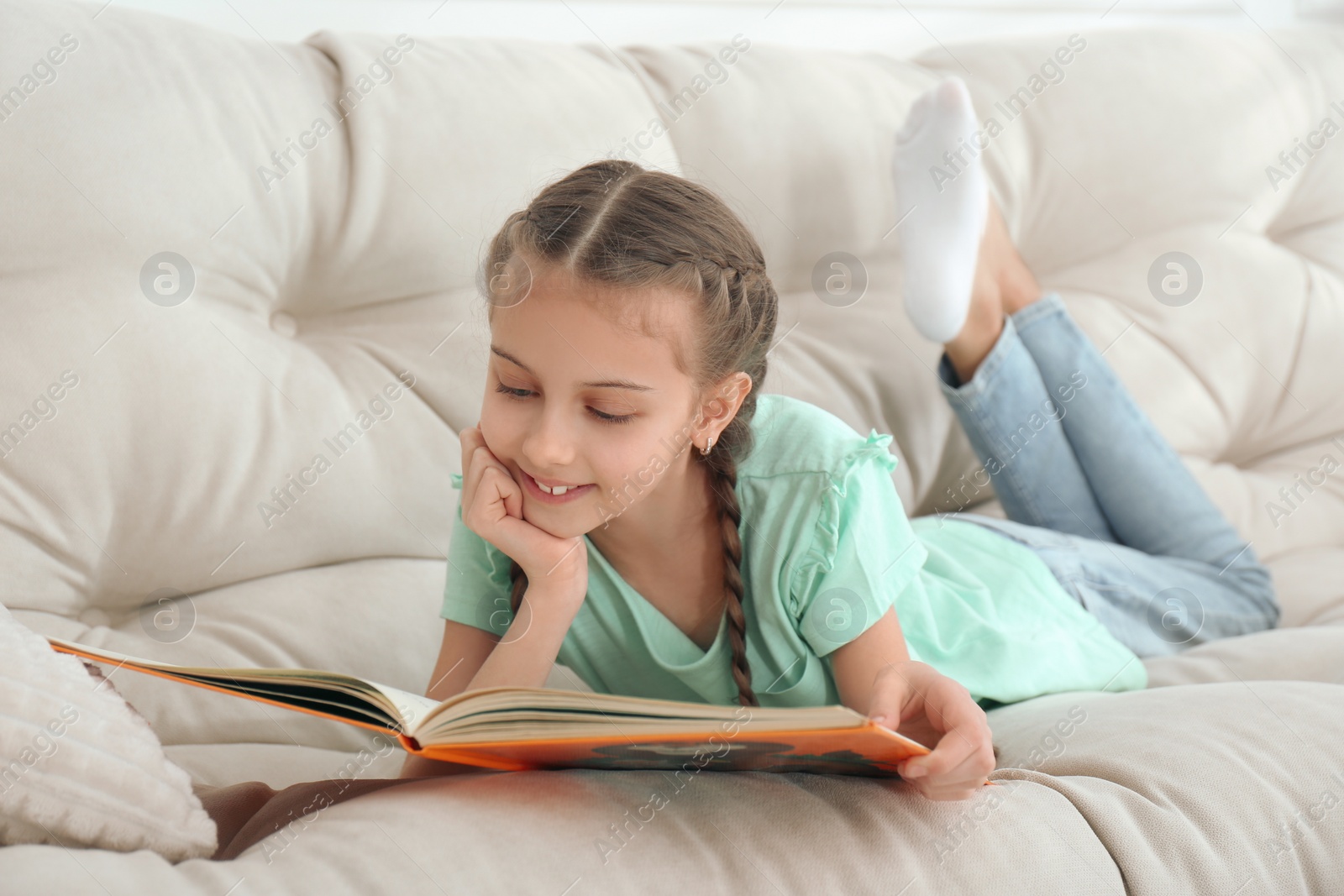 Photo of Cute little girl reading book on sofa at home