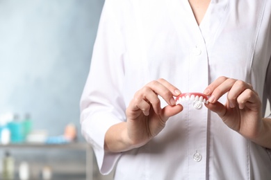 Photo of Dentist holding teeth cover on blurred background, closeup. Space for text