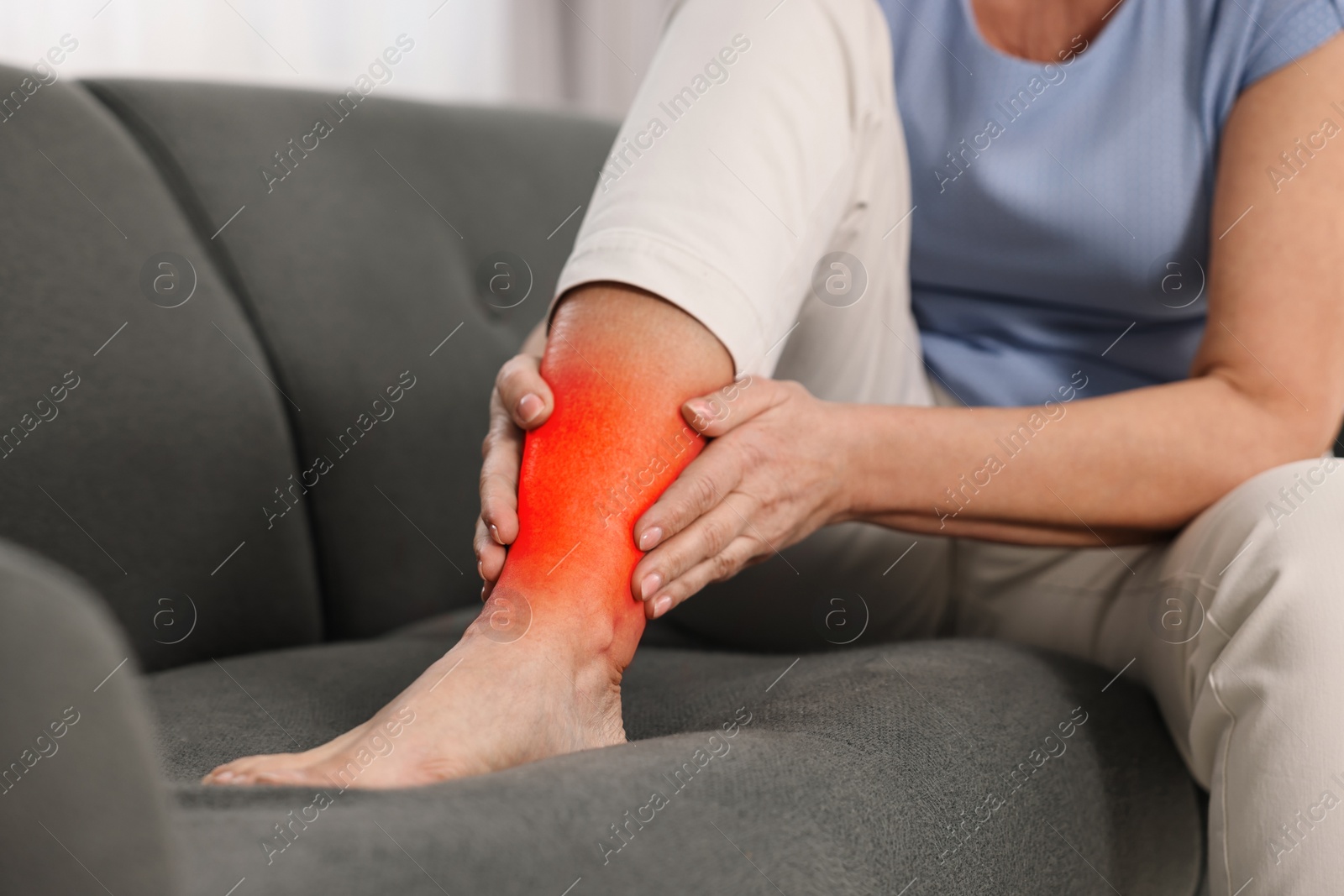 Image of Arthritis symptoms. Woman suffering from pain in her leg on sofa indoors, closeup