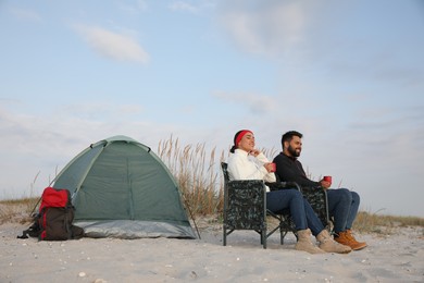 Couple with hot drinks near camping tent on beach