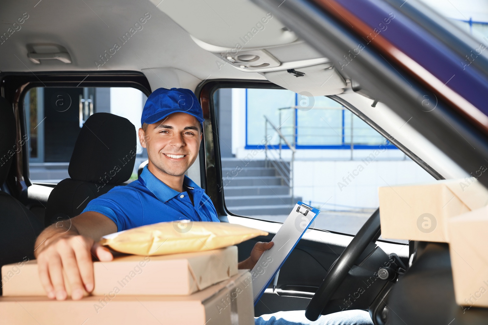 Photo of Young courier with clipboard and parcels in delivery car