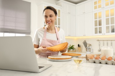 Woman making cake while watching online cooking course via laptop in kitchen