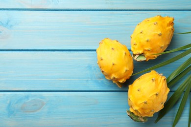 Photo of Delicious yellow pitahaya fruits with palm leaf on light blue wooden table, flat lay. Space for text