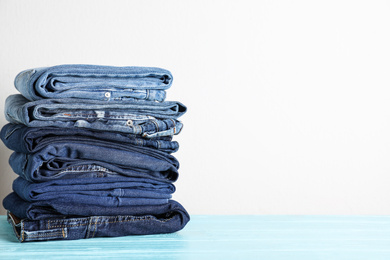 Stack of different jeans on blue wooden table. Space for text