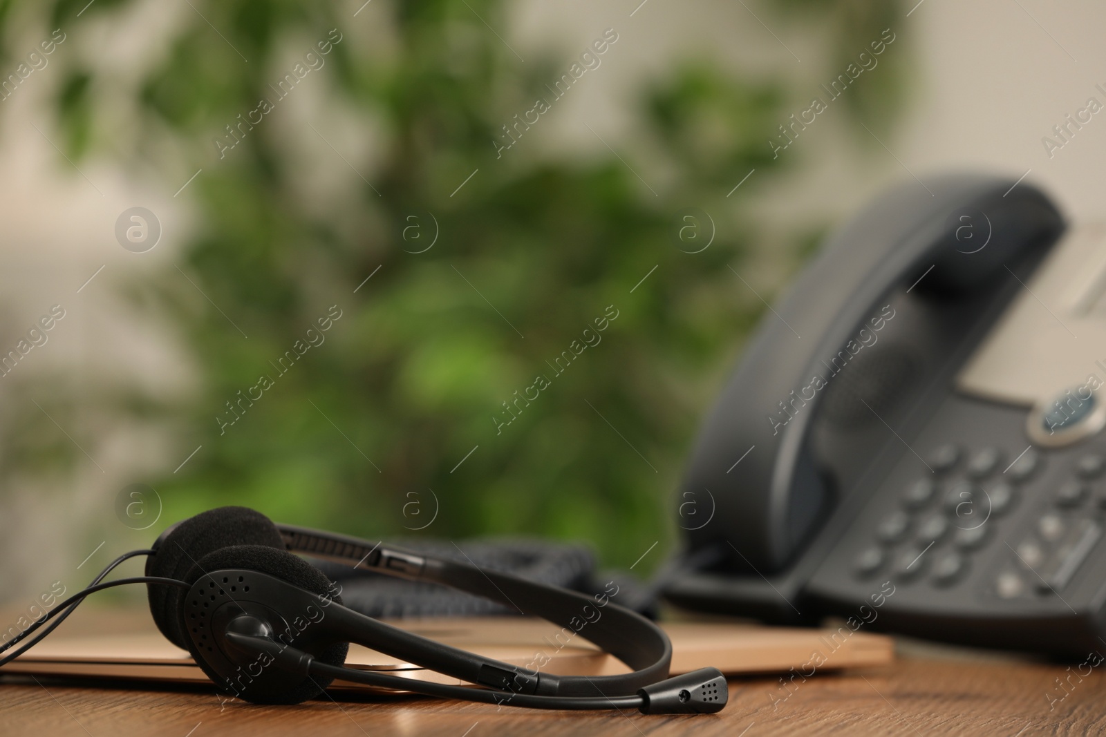 Photo of Headset, desktop telephone and laptop on table indoors, space for text. Hotline concept