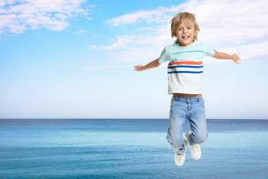 Image of Happy school boy jumping near sea, space for text. Summer holidays