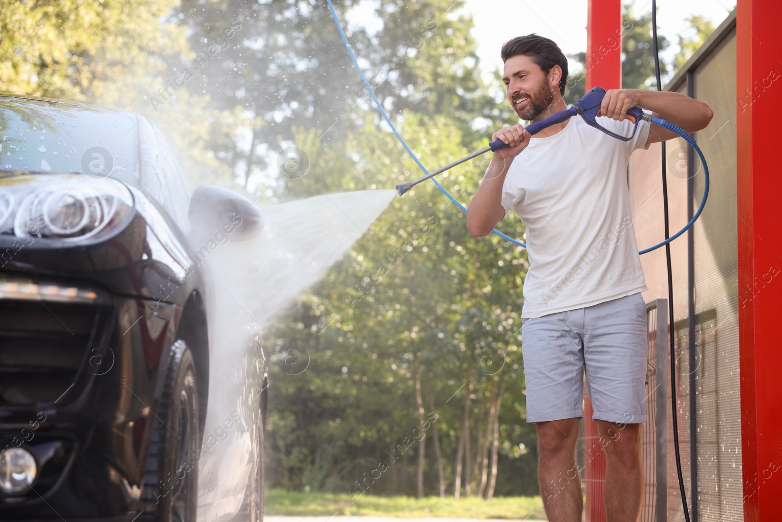 Photo of Happy man washing auto with high pressure water jet at outdoor car wash