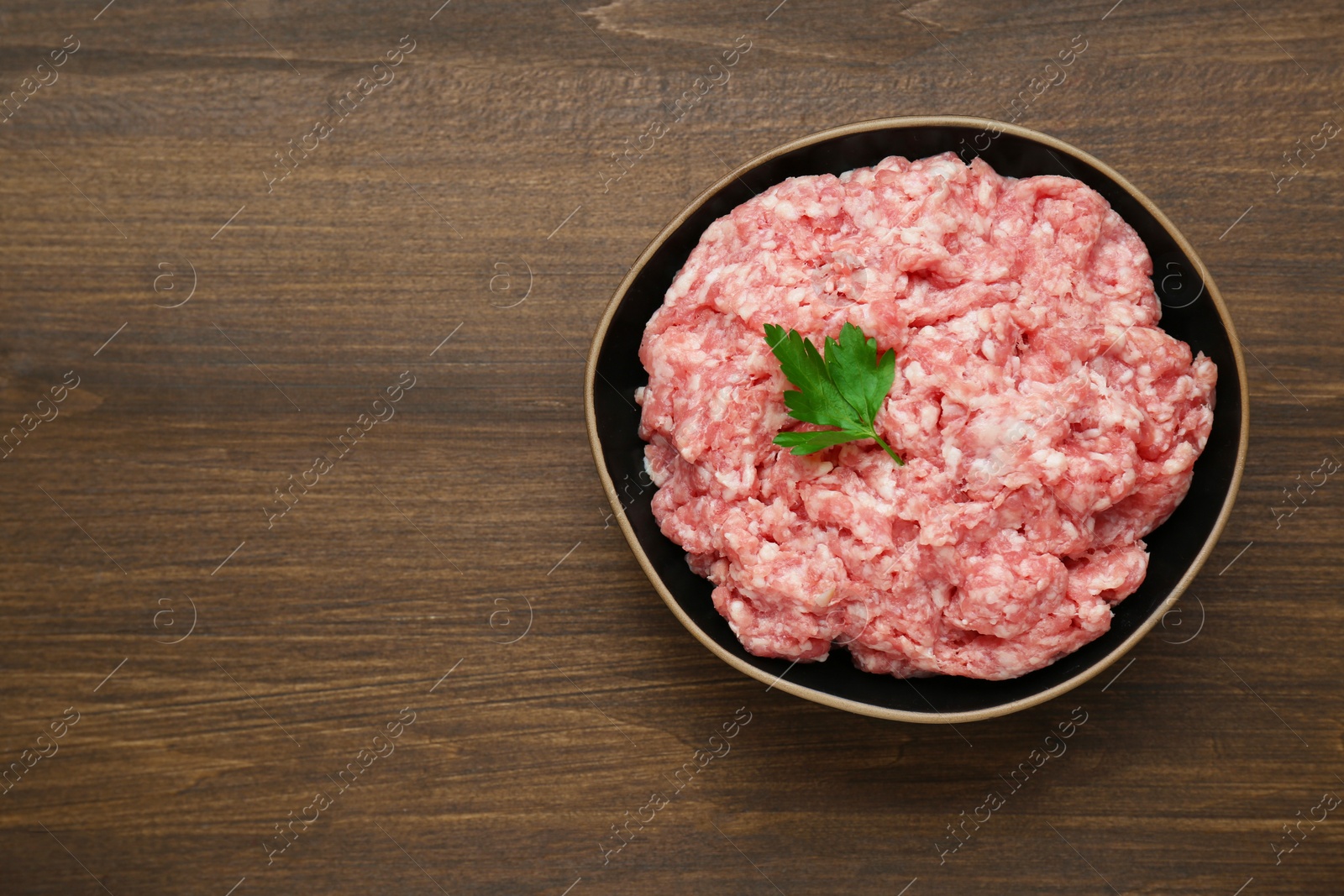 Photo of Bowl of raw fresh minced meat with parsley on wooden table, top view. Space for text