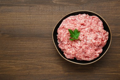 Bowl of raw fresh minced meat with parsley on wooden table, top view. Space for text