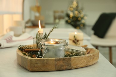 Burning scented conifer candle on white table indoors