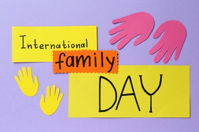Photo of Happy International Family Day. Cards with text and paper hands cutouts on violet background, flat lay