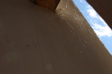 Cobweb on beige wall outdoors, low angle view. Space for text