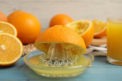 Photo of Fresh oranges and squeezer on blue wooden table, closeup