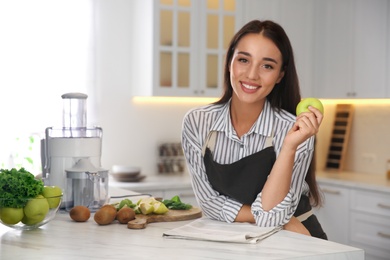 Photo of Young woman with fresh apple at table in kitchen. Preparing juice