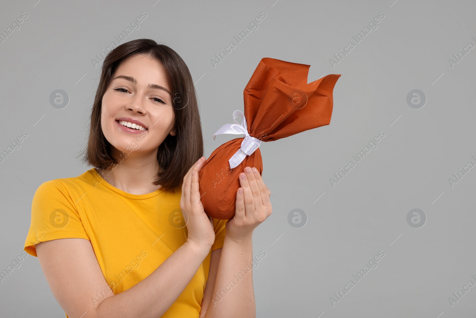 Photo of Easter celebration. Happy woman with wrapped egg on grey background, space for text