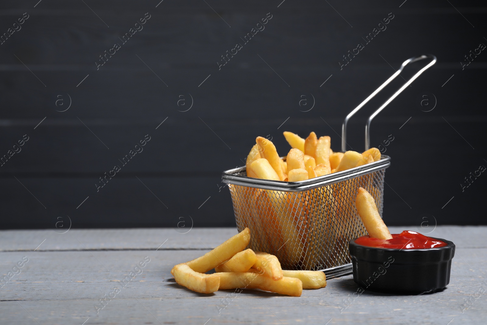 Photo of Tasty French fries served with ketchup on grey wooden table. Space for text