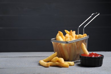 Photo of Tasty French fries served with ketchup on grey wooden table. Space for text