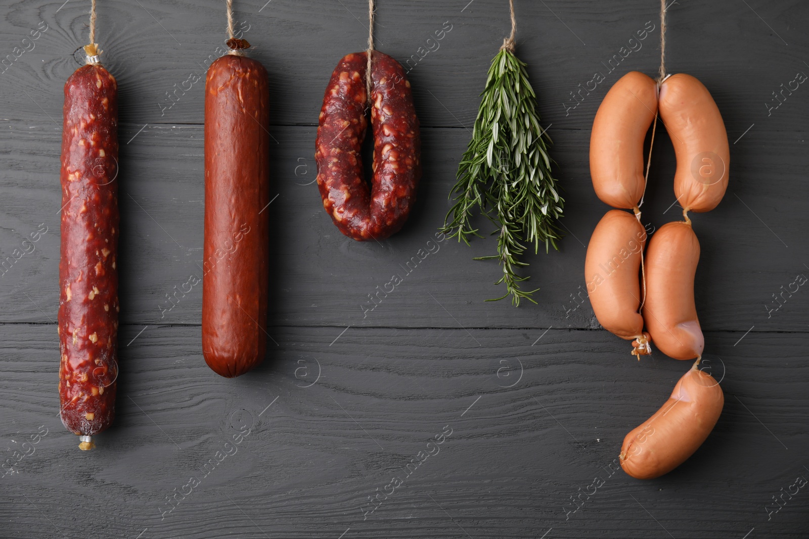 Photo of Different delicious sausages and bunch of rosemary hanging near dark grey wooden wall