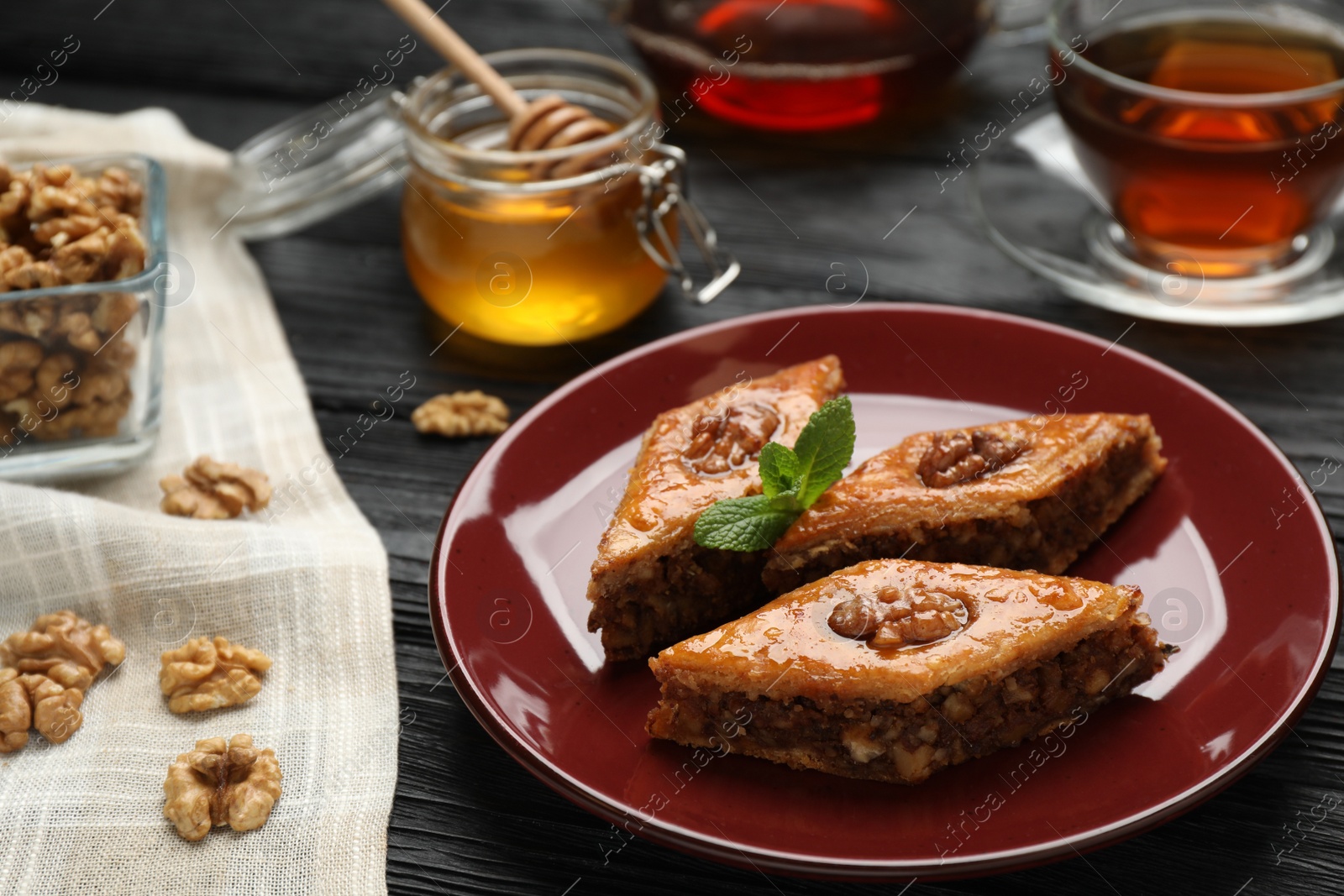 Photo of Delicious sweet baklava with walnuts and mint on black wooden table, closeup