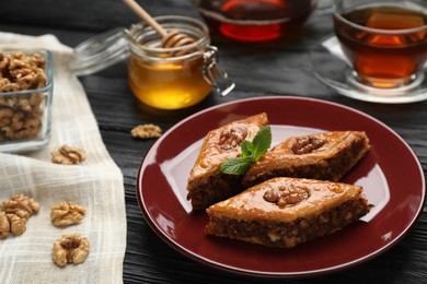 Delicious sweet baklava with walnuts and mint on black wooden table, closeup