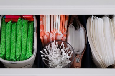 Photo of Open cabinet drawer with menstrual pads, tampons and cotton buds, above view