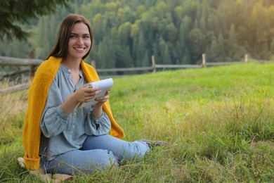 Photo of Beautiful young woman drawing with pencil in notepad on green grass