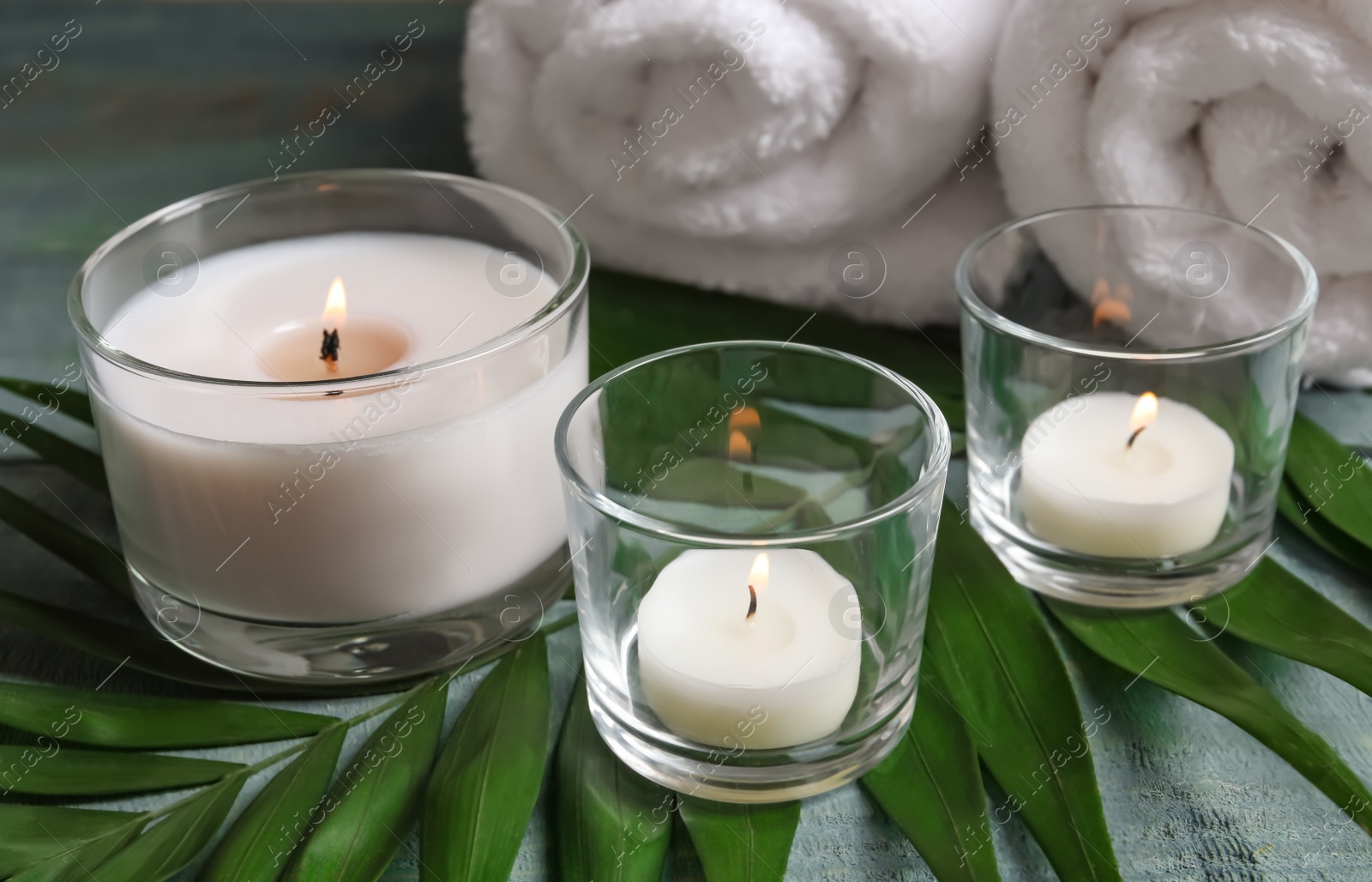 Photo of Spa composition with burning wax candles, towels and tropical leaf on table