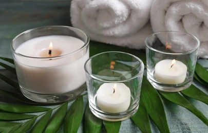 Photo of Spa composition with burning wax candles, towels and tropical leaf on table