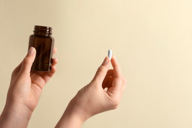 Woman holding pill and bottle on beige background, closeup. Space for text