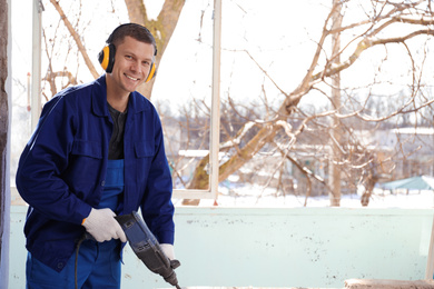 Photo of Worker using rotary drill hammer for window installation indoors