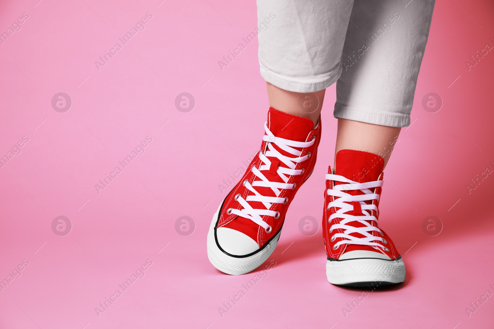 Photo of Woman wearing pair of new stylish sneakers on pink background, closeup. Space for text