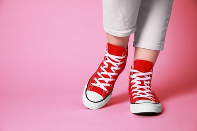 Woman wearing pair of new stylish sneakers on pink background, closeup. Space for text