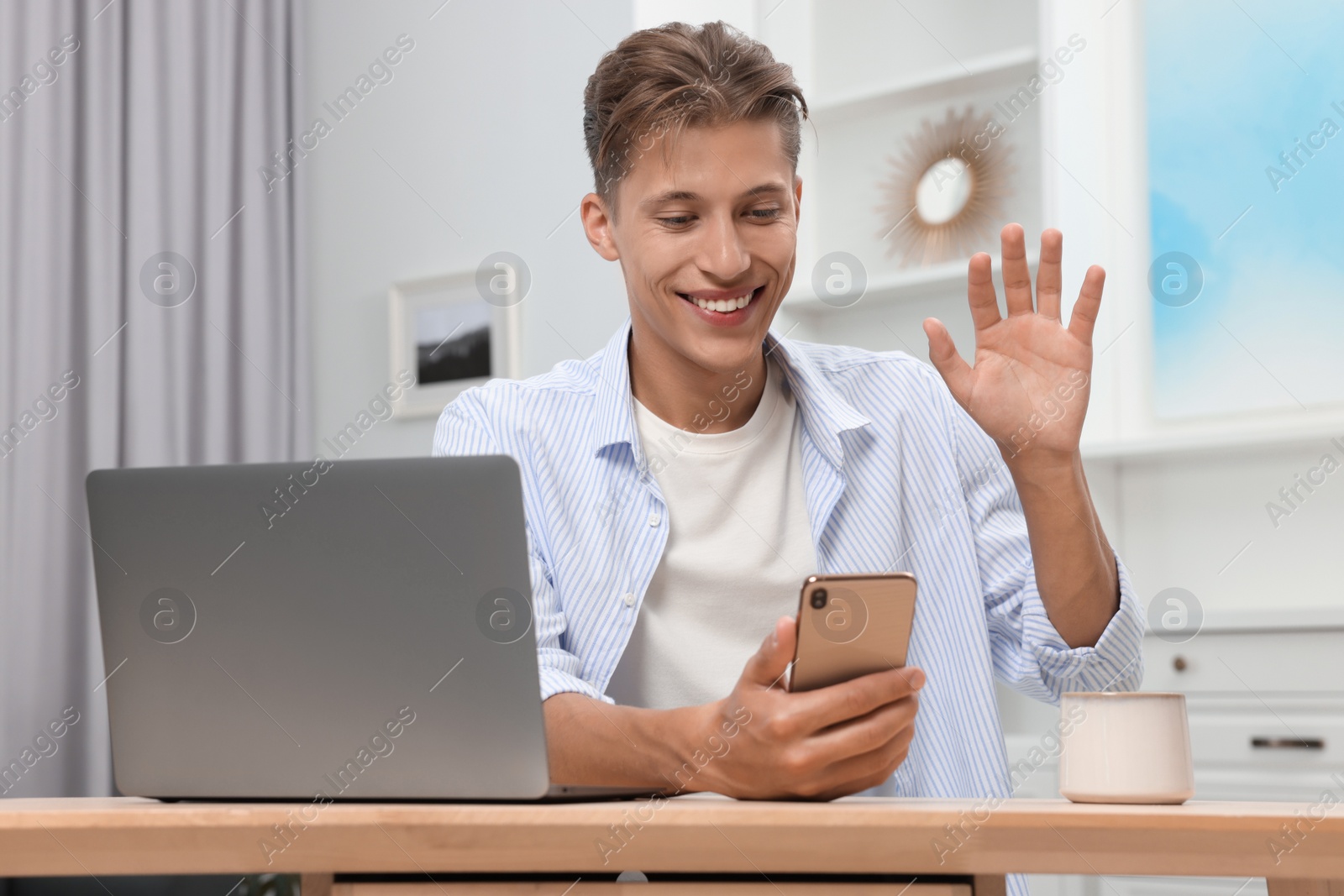 Photo of Happy young man having video chat via smartphone at wooden table indoors