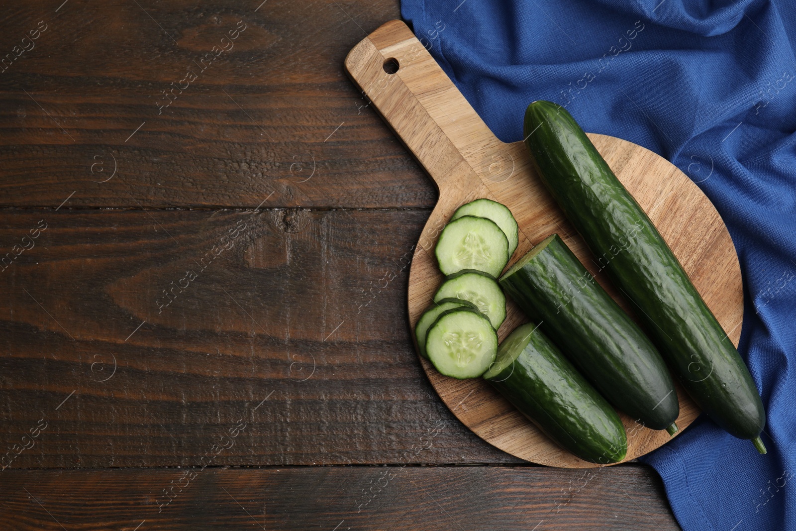 Photo of Fresh whole and cut cucumbers on wooden table, top view. Space for text