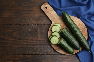 Fresh whole and cut cucumbers on wooden table, top view. Space for text