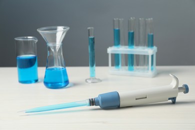 Photo of Laboratory analysis. Micropipette and different glassware with liquids on white wooden table