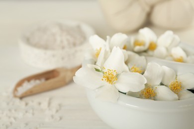 Mortar with beautiful jasmine flowers and pestle on white table, closeup. Space for text