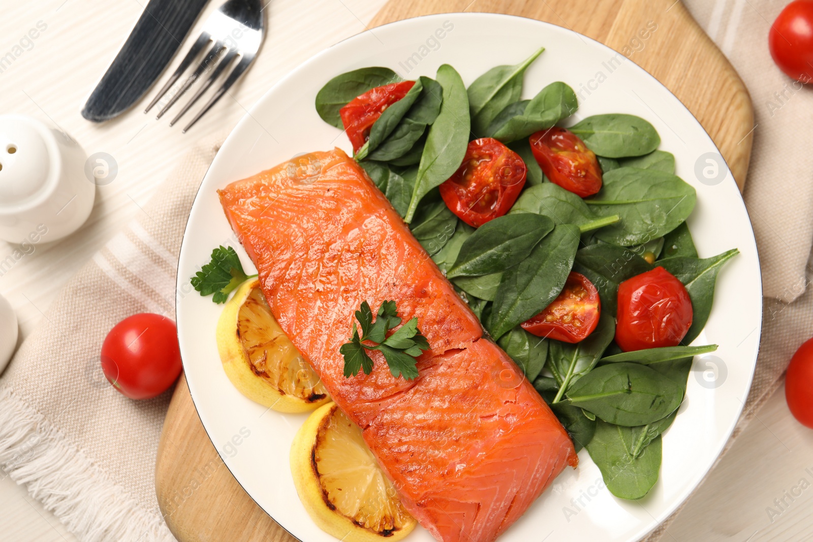 Photo of Tasty grilled salmon with basil, tomatoes and lemon on white wooden table, flat lay