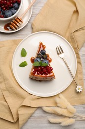 Slice of delicious cheesecake served with berries and caramel sauce on white wooden table, flat lay