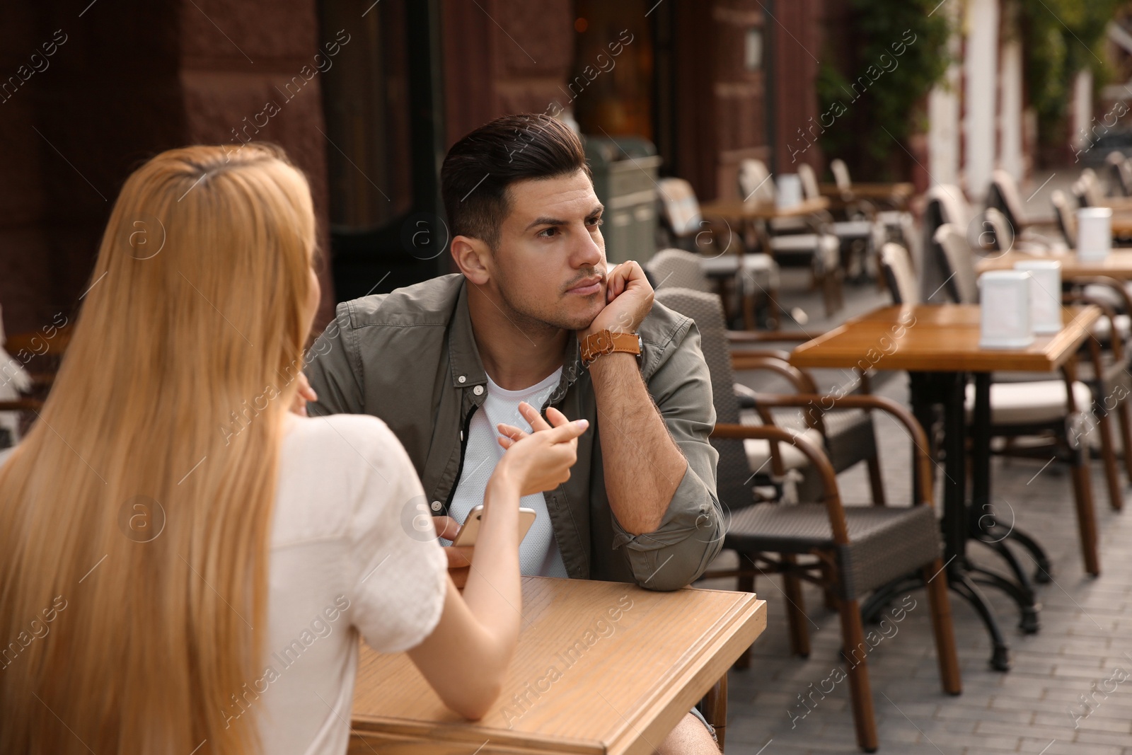 Photo of Man getting bored during first date with overtalkative young woman at outdoor cafe