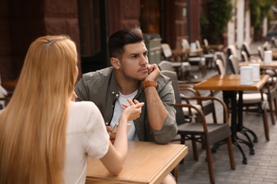 Photo of Man getting bored during first date with overtalkative young woman at outdoor cafe