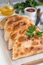 Photo of Board with delicious fried chebureki and parsley on white table, closeup
