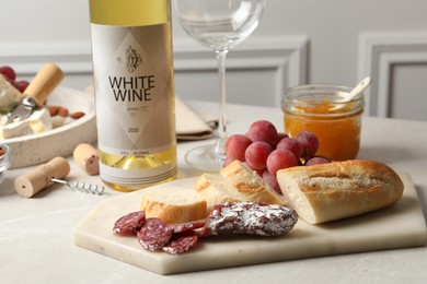 Bottle of white wine, glass and snacks on table, closeup