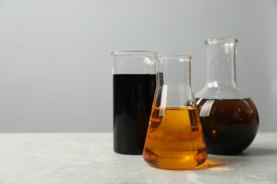 Beaker and flasks with different types of oil on white table, space for text