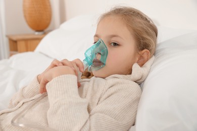 Photo of Little girl using nebulizer for inhalation in bedroom