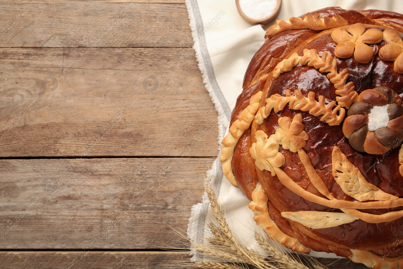 Photo of Korovai with wheat spikes on wooden table, space for text. Ukrainian bread and salt welcoming tradition