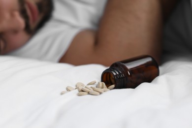Photo of Man sleeping on bed, closeup. Overturned bottle with antidepressants, selective focus