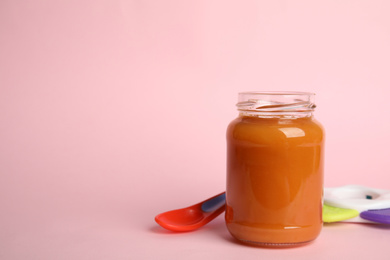 Photo of Jar with healthy baby food, spoon and toy on pink background, space for text