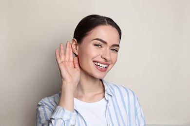 Photo of Young woman showing hand to ear gesture on light background