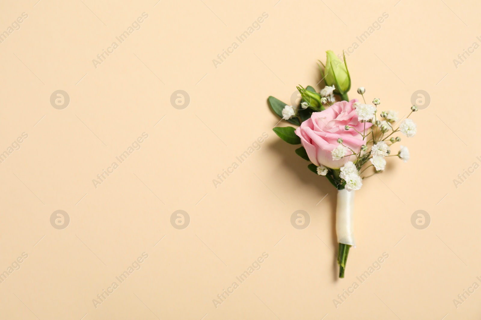 Photo of Wedding stuff. Stylish boutonniere on beige background, top view. Space for text
